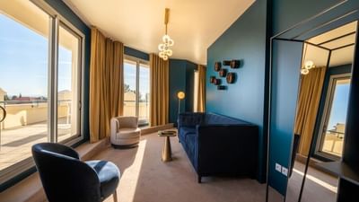 A room with a balcony, blue couch, chairs, round table, and large mirror.