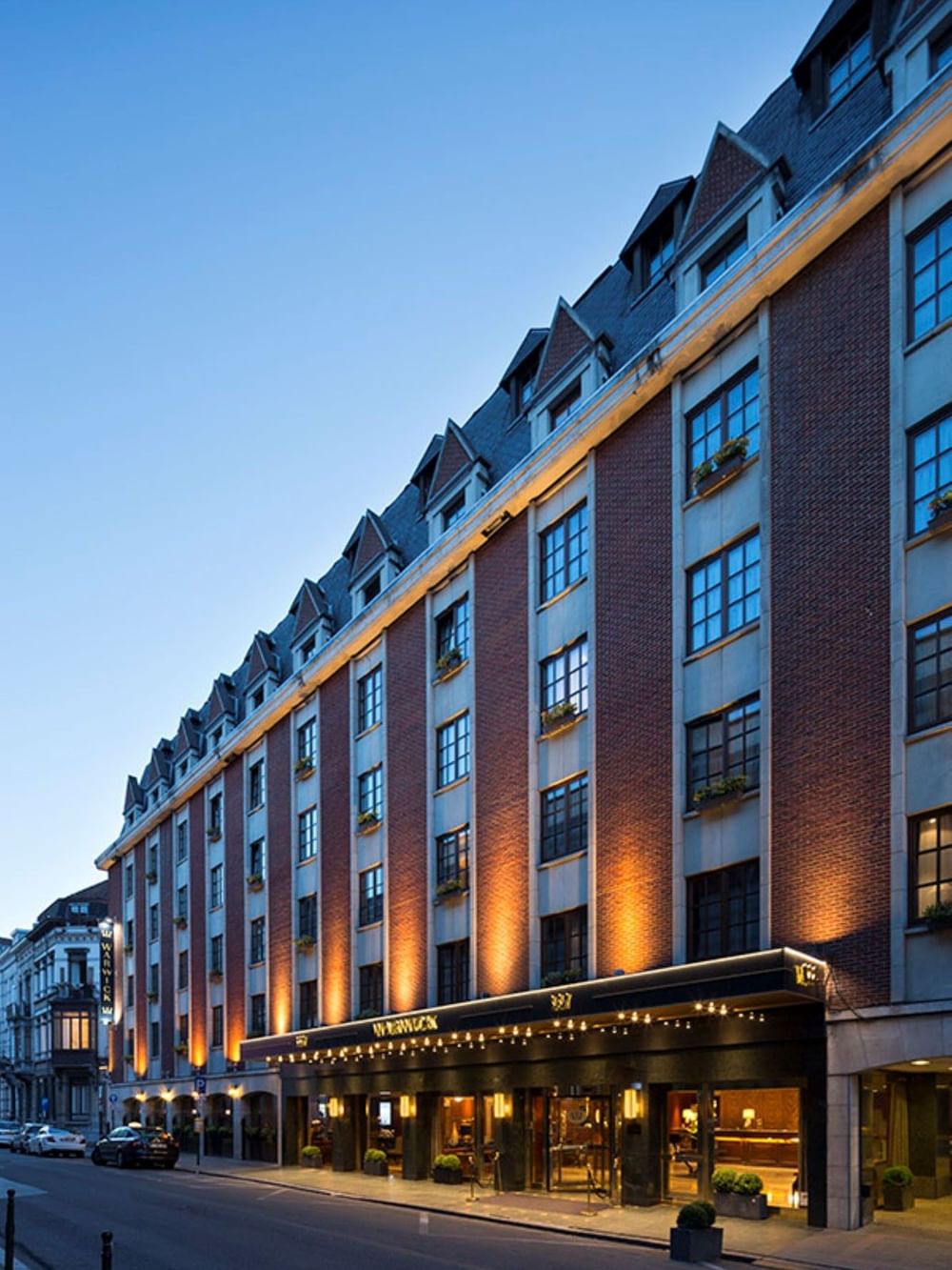 Façade élégante d'un hôtel illuminé au crépuscule avec marquise dorée et architecture en brique à Bruxelles.