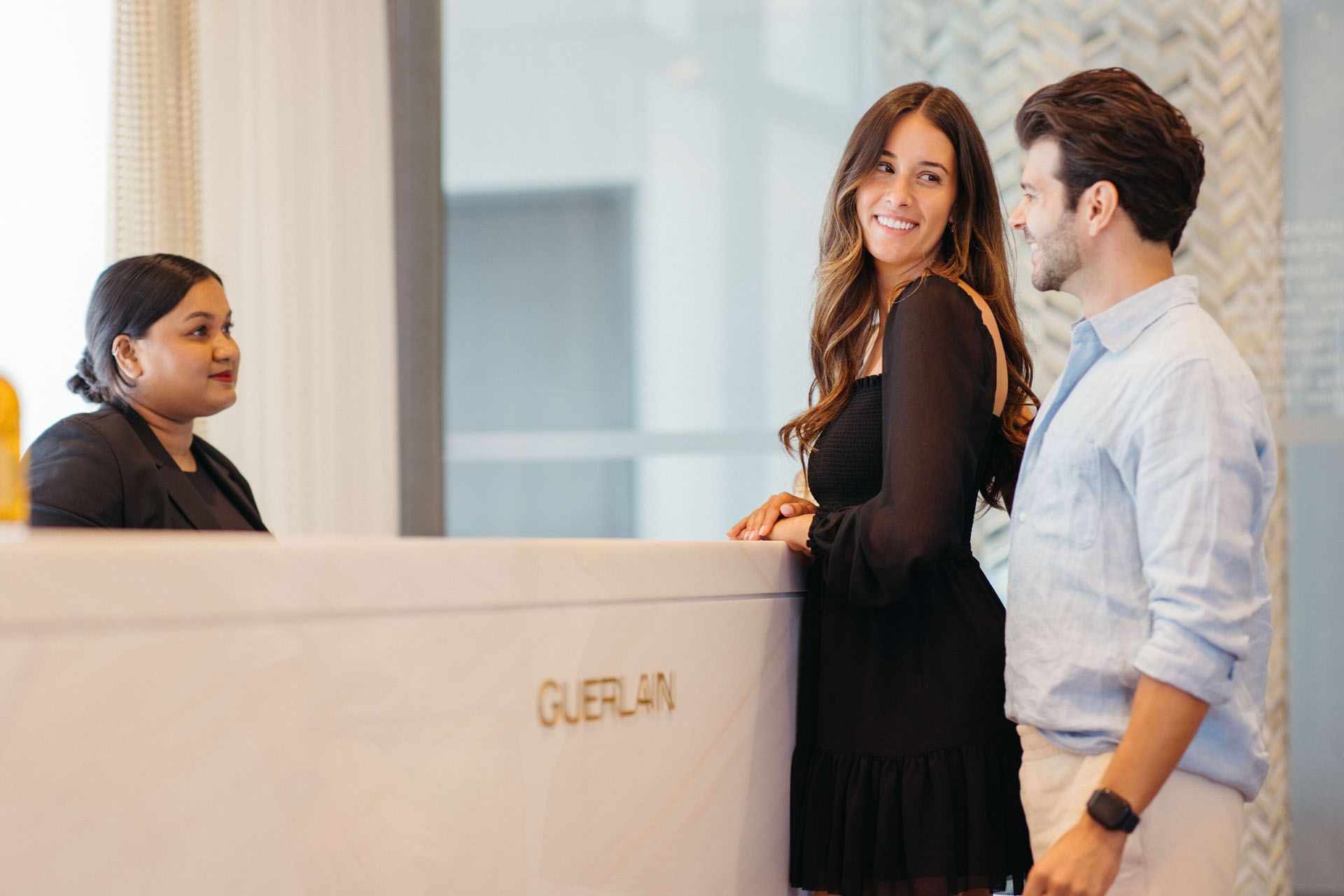 Couple standing at a white marble reception counter chatting with a receptionist at Guerlain Spa at Hotel X Toronto