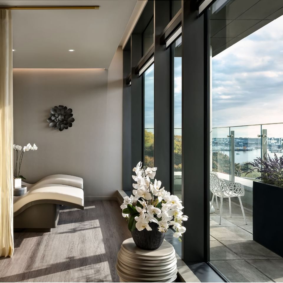 White spa lounger by orchids and floor-to-ceiling windows overlooking the waterfront in Guerlain Spa at Hotel X Toronto