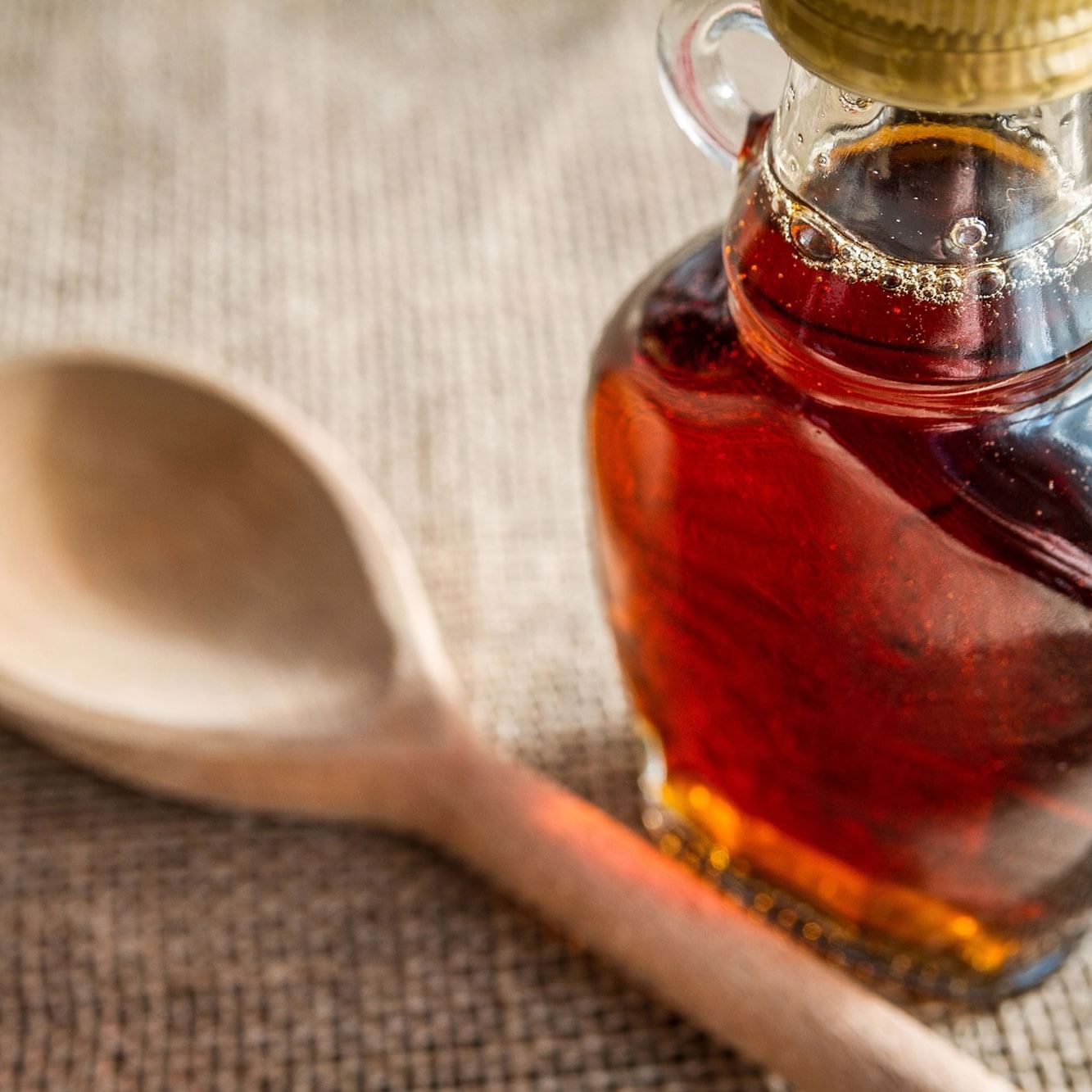 Glass bottle of maple syrup with a wooden spoon.