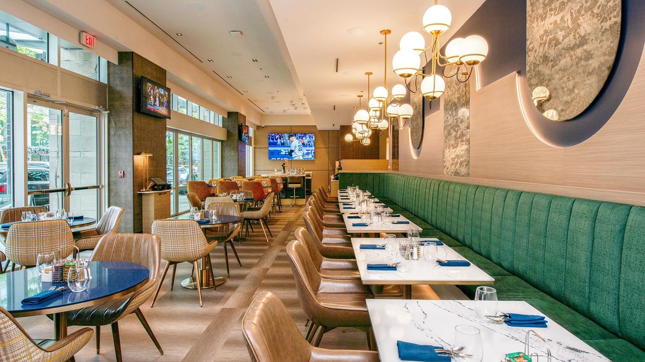Restaurant with green banquette seating, chairs, and elegant lighting.