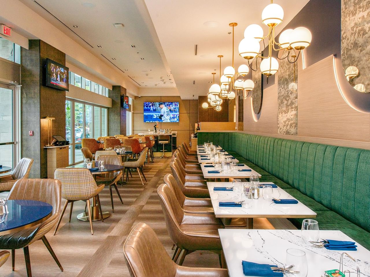 Restaurant with green banquette seating, chairs, and elegant lighting.