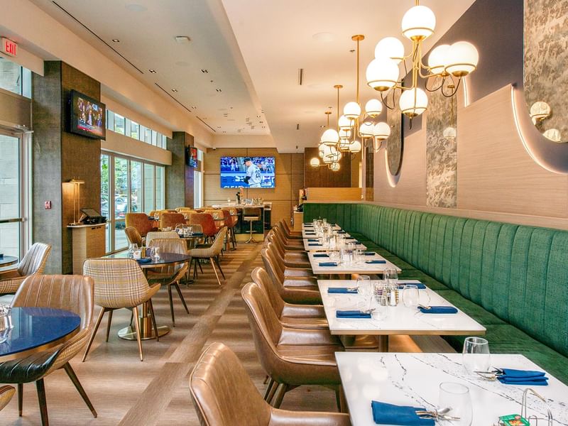 Restaurant with green banquette seating, chairs, and elegant lighting.