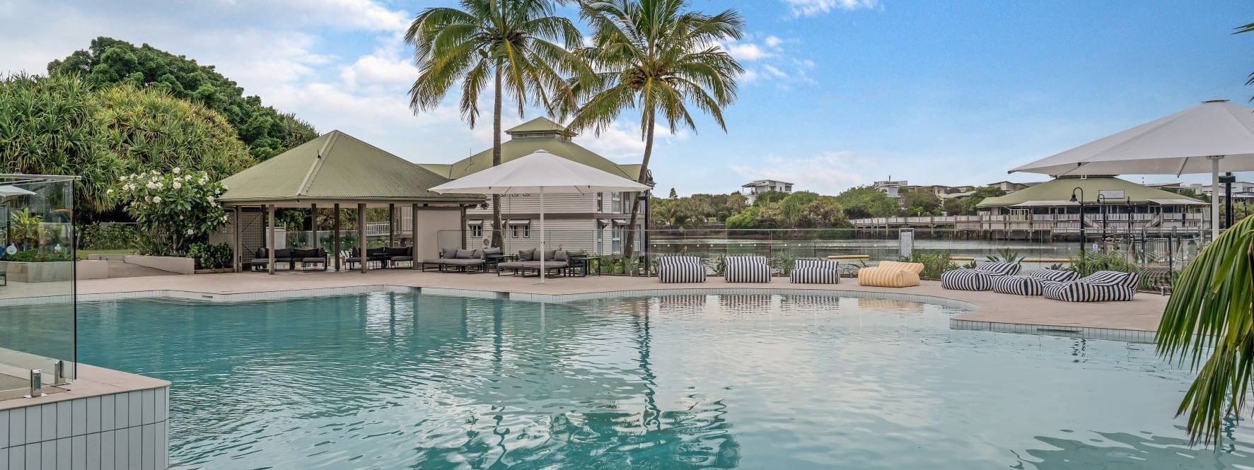 Lounge chairs and shaded cabanas by the pool, surrounded by palm trees at Novotel Sunshine Coast Resort