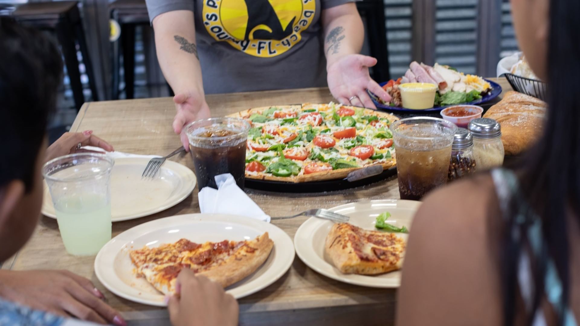 Woman serving pizza to the table with drinks and salad dishes in Bruno’s Pizzas Watersound Inn