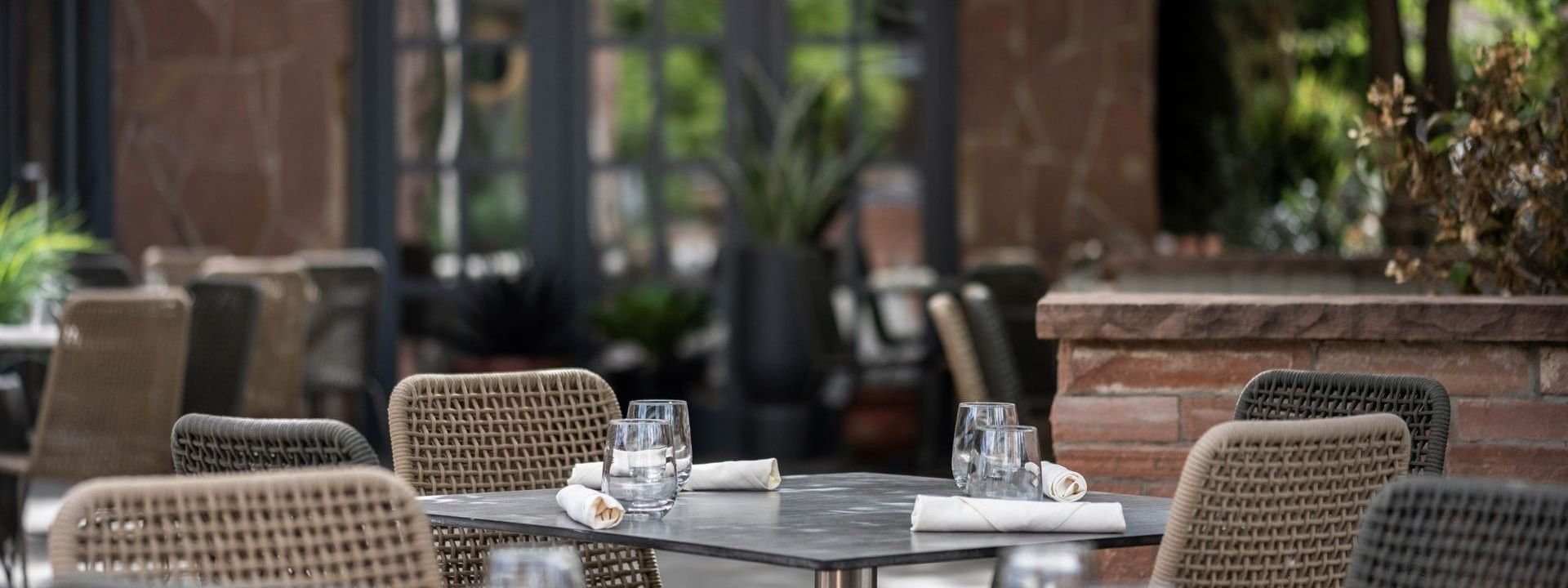 Woven chairs by tables with white linens under leafy green tree branches in Gattara Restaurant & Patio at Warwick Denver