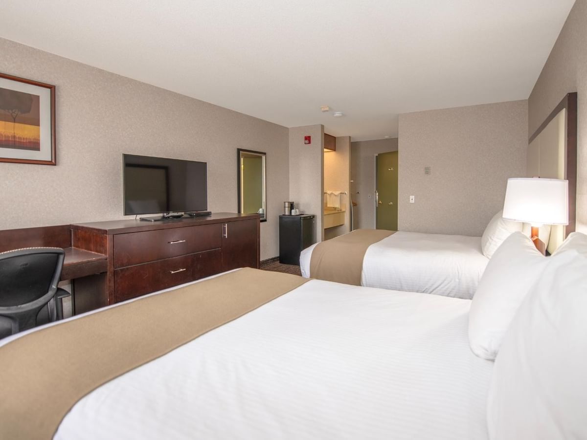 A hotel room with two beds, a desk, a chair, a TV, a lamp, and a picture frame.