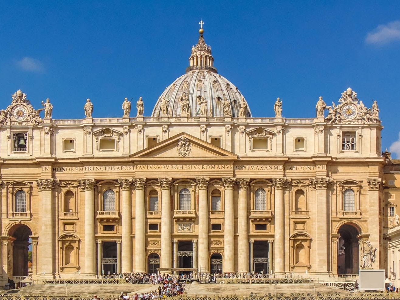 St. Peter's Basilica facade with detailed sculptures set against a bright blue sky near The Guardian Hotel