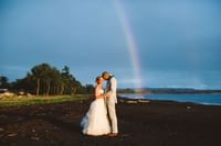 wedding photo on the beach located at Waimea Plantation Cottages with a rainbow in the background