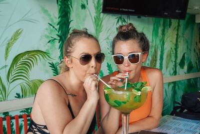 Two women drinking a Mojito from a large glass with straws at Fairwind Hotel Miami