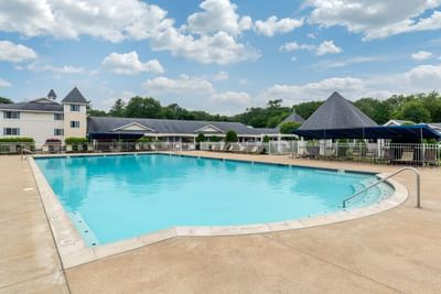 Bright blue pool with lounge chairs and canopies under a cloudy sky at Ogunquit Hotel and Suites