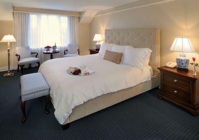 Guest bedroom featuring a plush king bed with a breakfast tray beside striped armchairs and lamps at The Simsbury Inn