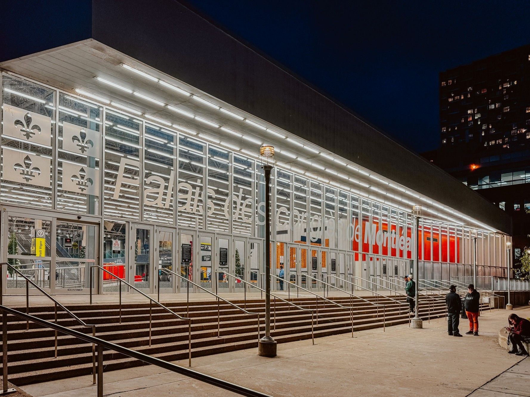 Palais des Congrès de Montréal illuminé la nuit avec des visiteurs à l'entrée.