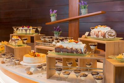 Dessert display featuring various cakes arranged on wooden stands in Delphos Bistro at Hotel Los Delfines & Casino
