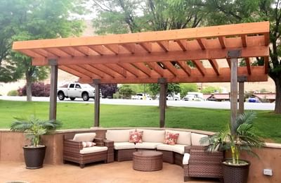 Cozy outdoor seating at Moab Valley Inn under a wooden pergola, with cushions, a coffee table, and lush greenery all around