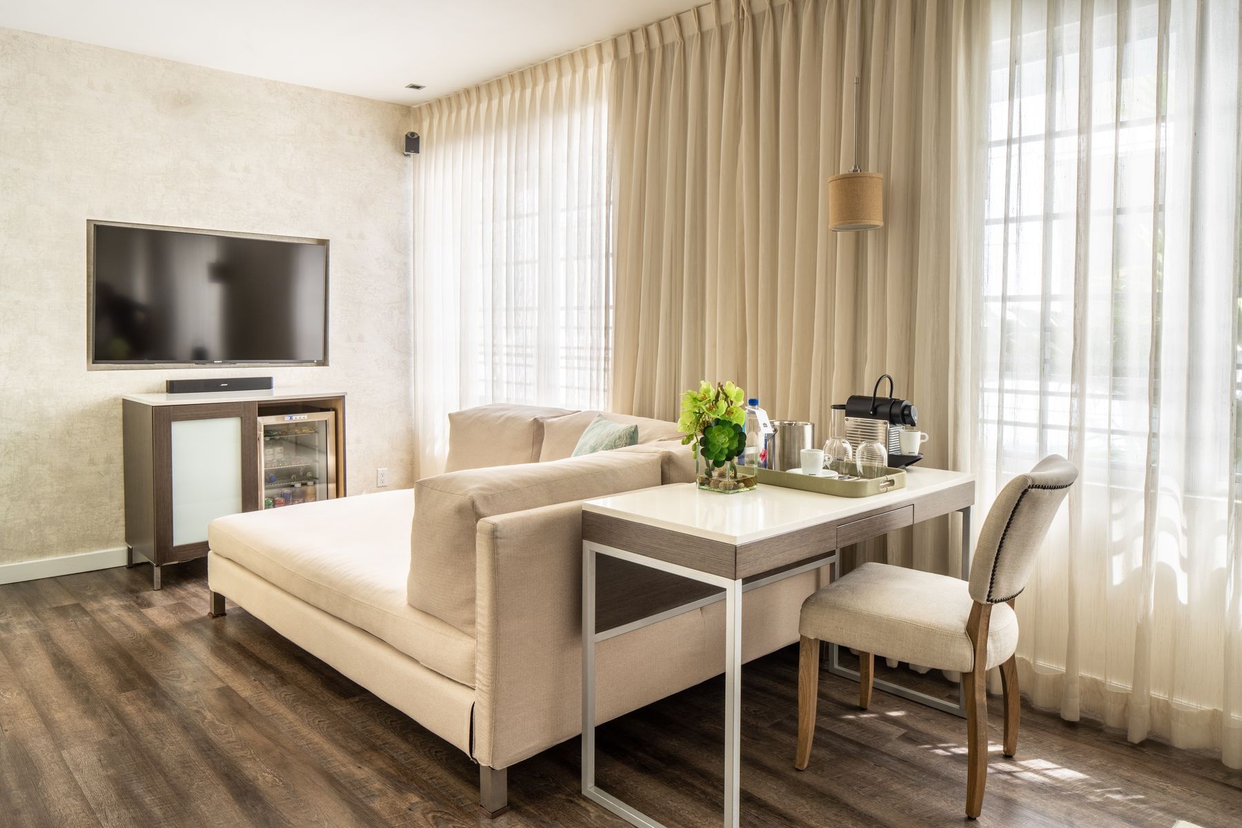 A wide view of a hotel suite with a sofa, coffee table, chair, TV, and refrigerator.