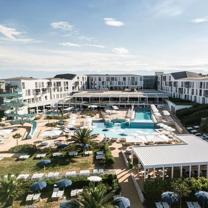 Vista aerea di un resort con piscine, scivolo, ombrelloni, edifici e vegetazione.