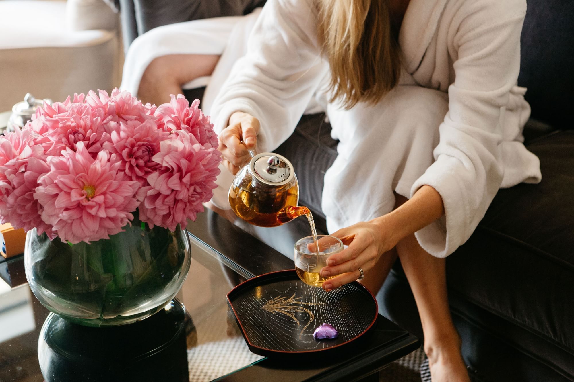 A person in a white robe pouring tea near a vase of pink flowers at Sofitel Brisbane Central