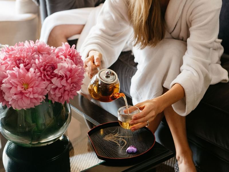 Woman in a white robe pouring tea at Stephanies Luxury Spa near Sofitel Brisbane Central