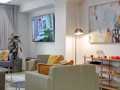 Modern lounge area with gray sofas, yellow cushions, wall-mounted TV, and colorful artwork at UniLodge Auckland Central