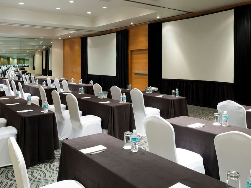 Classroom setup in Nueva York Venue with black linens, white chairs, and large dual projection screens at Real Inn Perinorte