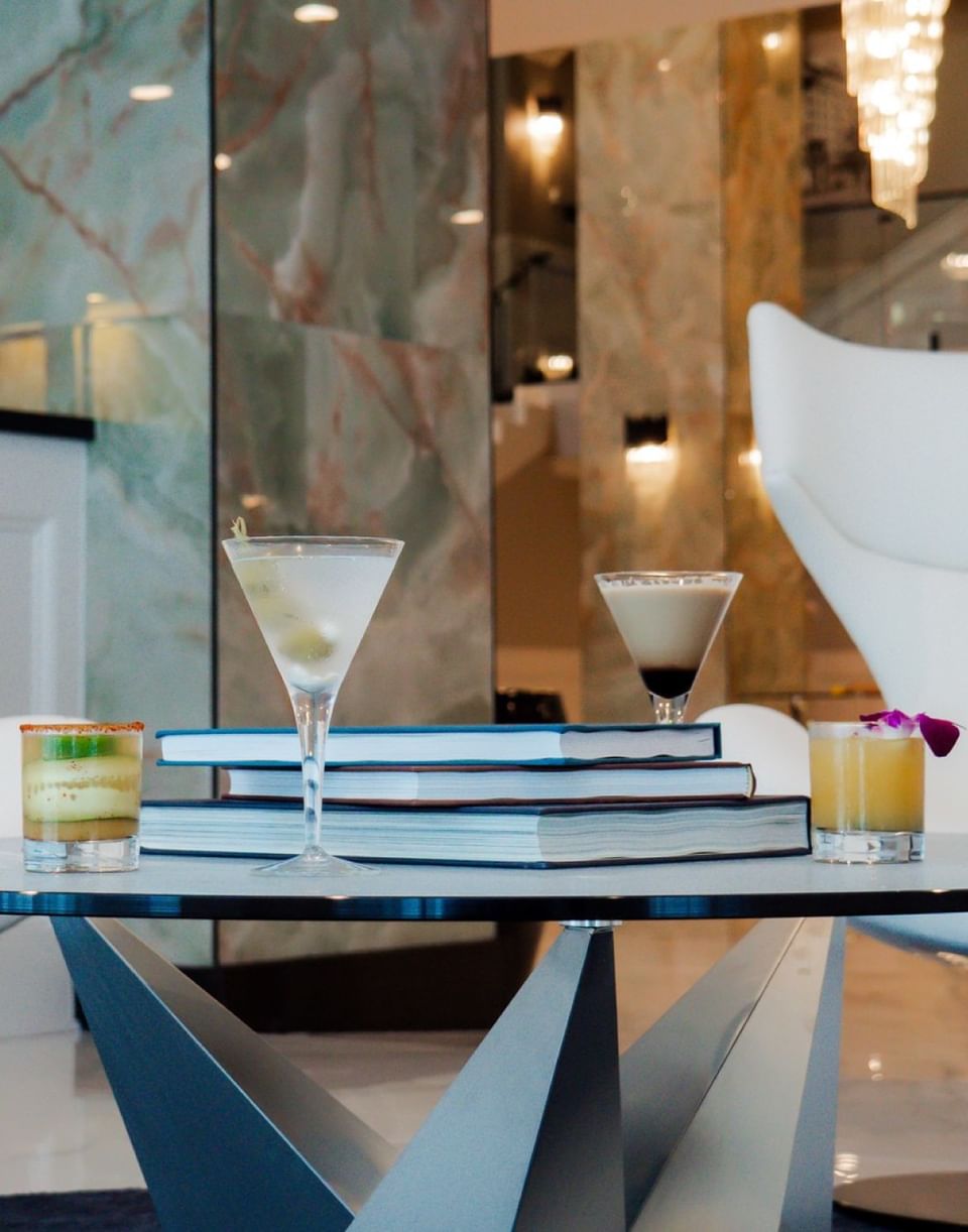 Assorted gourmet cocktails and martini glasses arranged on a table with blue art books at The Markham Hotel