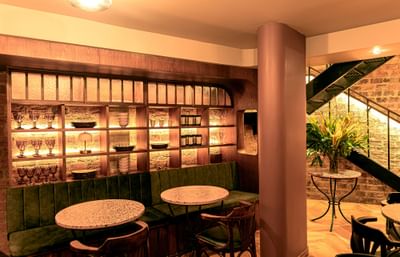 Green velvet booth by marble tables under a wooden display shelf and floral arrangements at 5Q House Chapinero