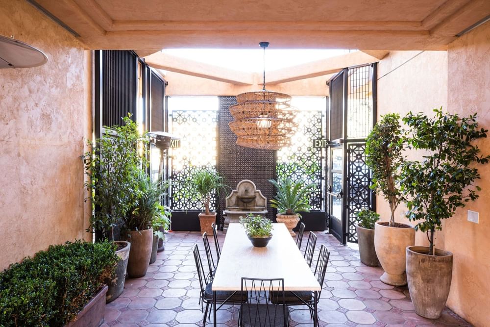 Outdoor dining area featuring a long table, a fountain, and lush potted plants at El Prado Hotel