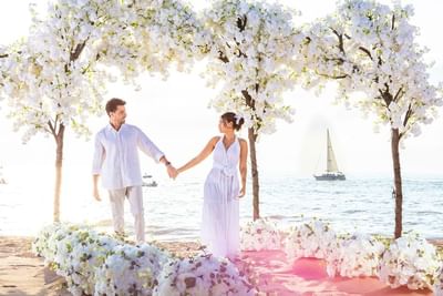 Couple holding hands at beachfront wedding ceremony with white floral arch and pink aisle at Playa Los Arcos Puerto Vallarta 2023