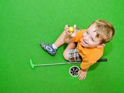 A kid sitting at Minature Golf Club ground near ICONA Windrift