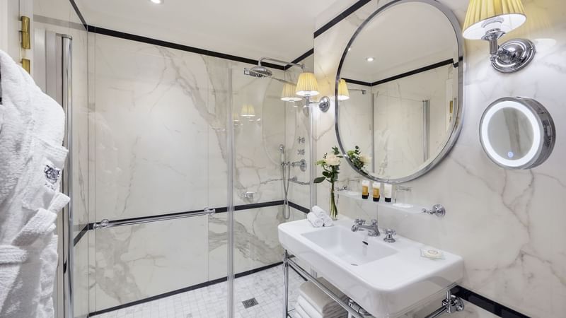 Superior Room bathroom with marble walls, glass shower and a round mirror at Hôtel Westminster - Paris