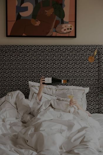 A person lying in bed with a bottle of champagne at The Sparrow Hotel