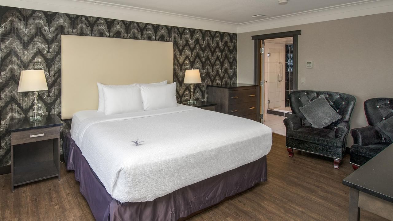 Modern hotel room with king bed, patterned accent wall, seating area, and hardwood floors at Coast Calgary University Area Hotel by APA