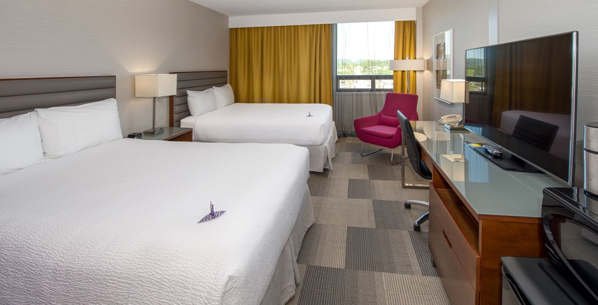 A hotel room with two beds, a desk with a TV, a chair, and a window with curtains.