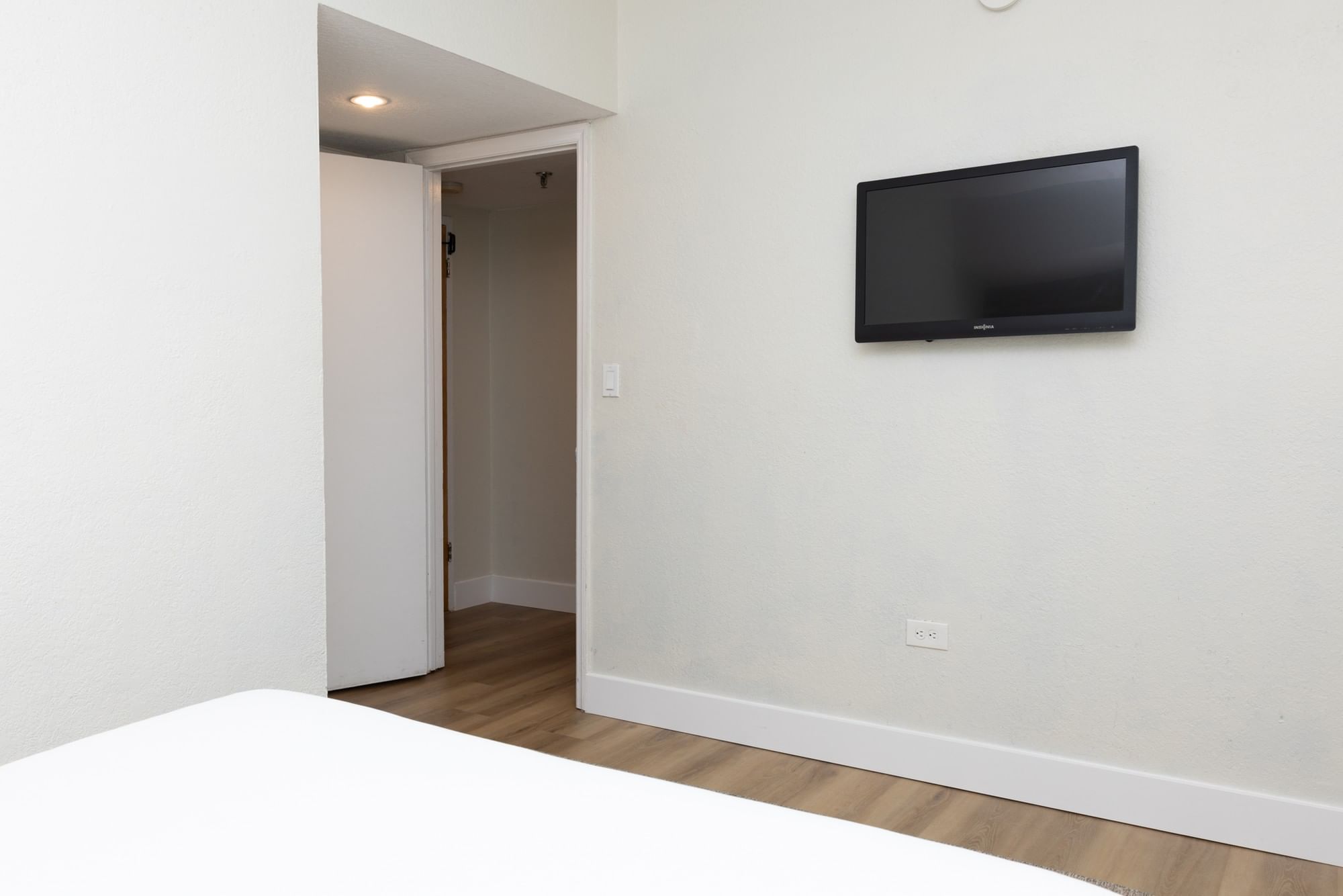 A hotel room with a TV on the wall, a doorway to another room, and a bed