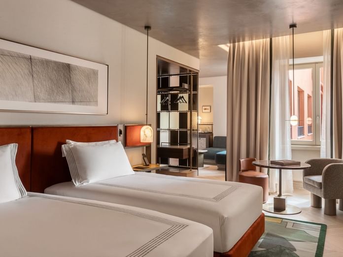 Two twin beds with wood headboards and white linens in a modern suite at The Thompson Rome, Roma.