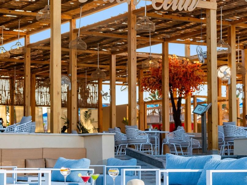 Outdoor beach club with white furniture, blue cushions, and a wooden canopy with 