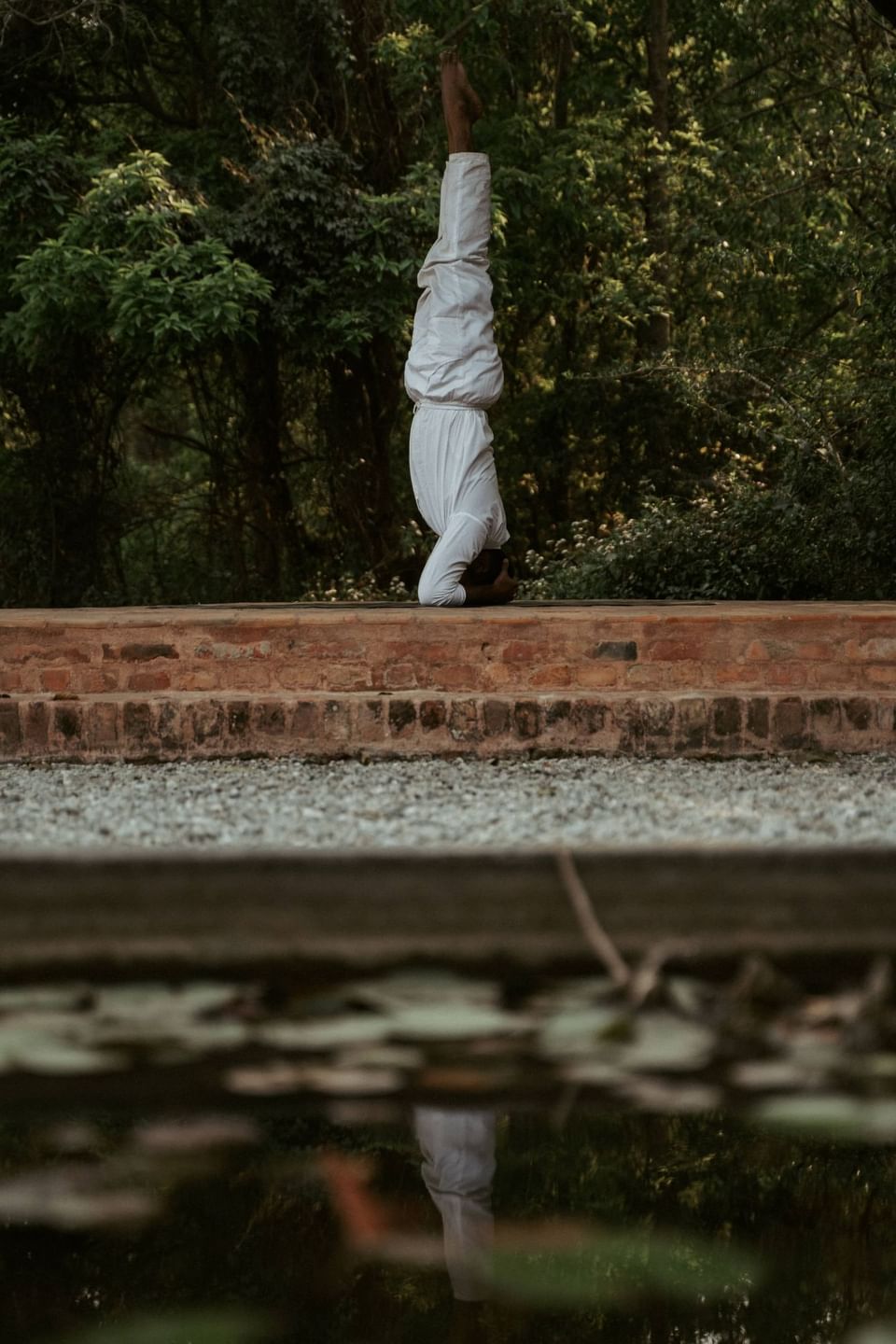 Person performs a headstand by a calm pond, surrounded by lush greenery at The Dwarika's Himalayan Wellbeing