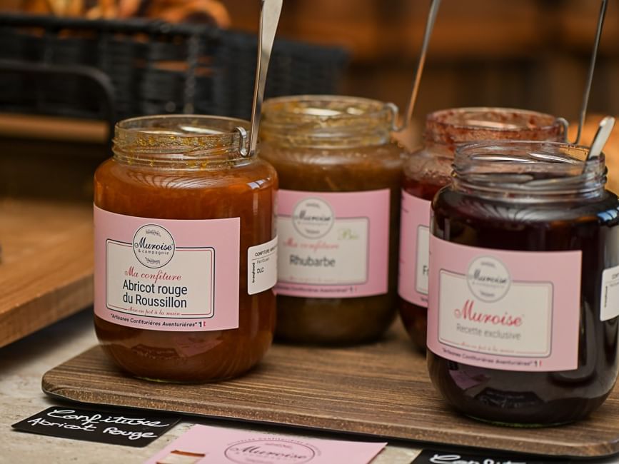 Quatre pots de confiture avec étiquettes roses sur planche en bois chez Hôtel Rivella.
