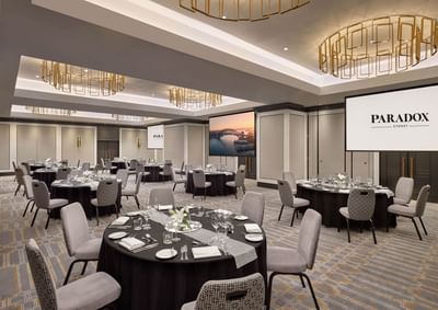Spacious conference room with round tables and large screens displaying hotel logo at Paradox Sydney conference room