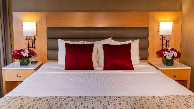 Room with a large bed, two nightstands, flowers, and a wooden headboard with lights at Warwick Hotels and Resorts