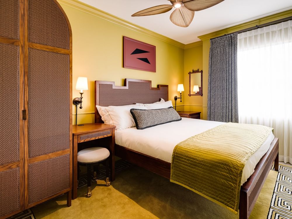 A hotel room with a king-sized bed, desk, wardrobe, and ceiling fan.