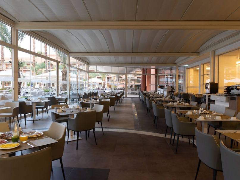 Interior of a spacious restaurant with many tables, chairs, and large windows overlooking an outdoor area.