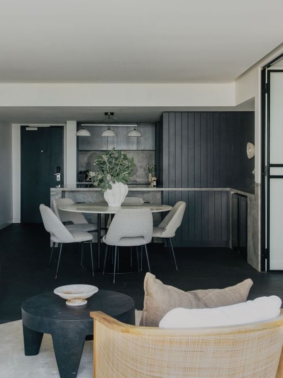 Elysium Suite at Elysium Manly, featuring a table and dining chairs under hanging lights, with a sofa in the foreground