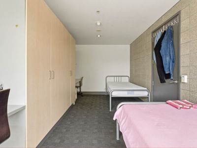 Two single beds with pink bedding and wardrobes in a room at Student Living Auckland - Beach.