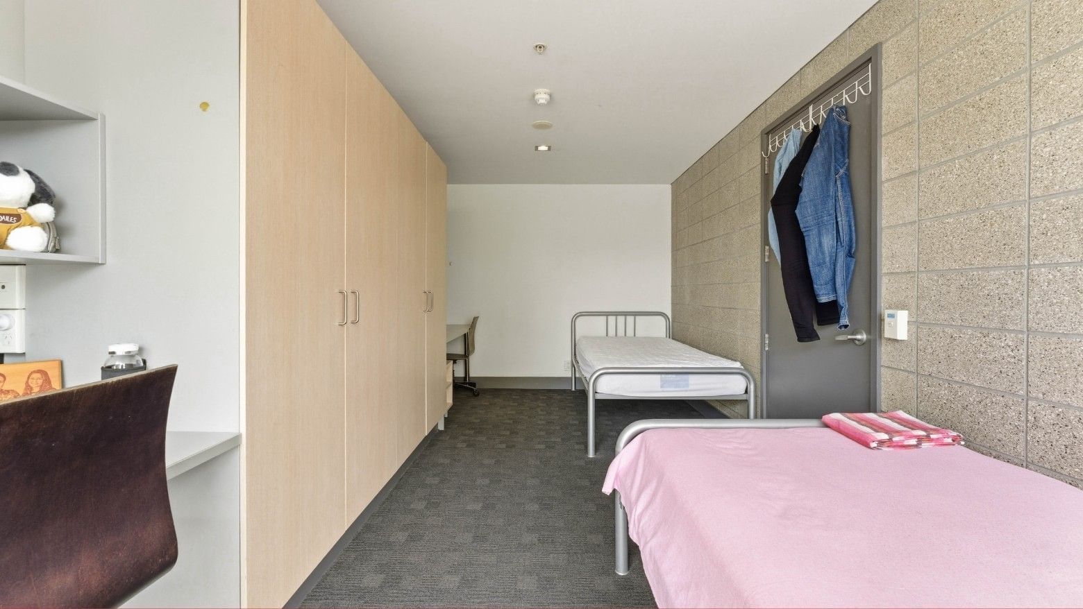 Two single beds with linens and closets in a room at Student Living Auckland - Beach.