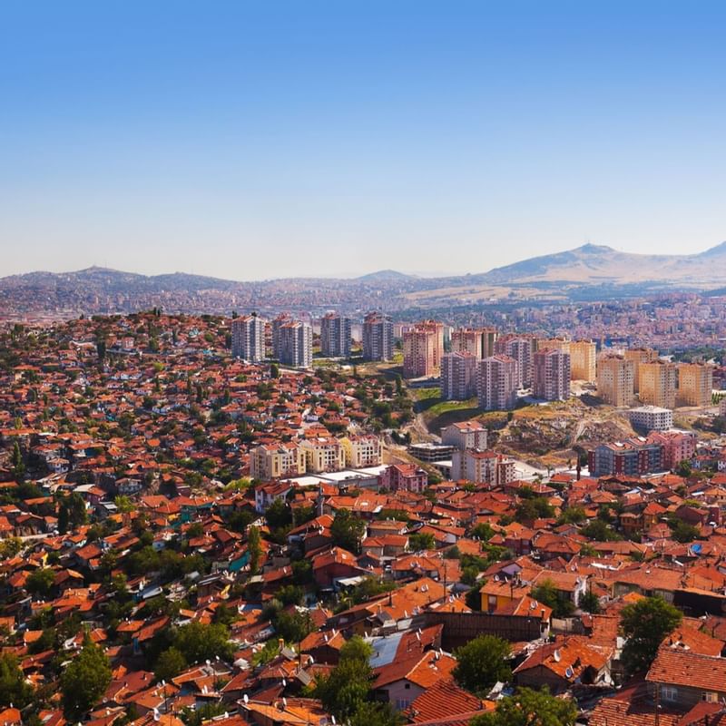 Panoramic view of Ankara city with numerous red-tiled roofs, modern buildings, and mountains near Warwick Hotels and Resorts