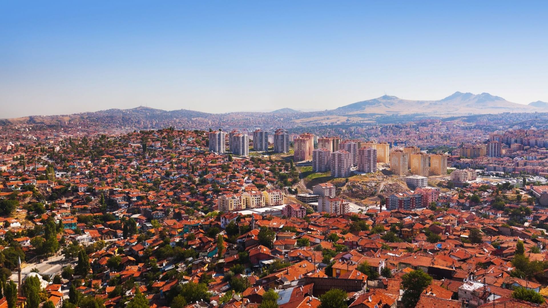 Panoramic view of Ankara city with numerous red-tiled roofs, modern buildings, and mountains near Warwick Hotels and Resorts