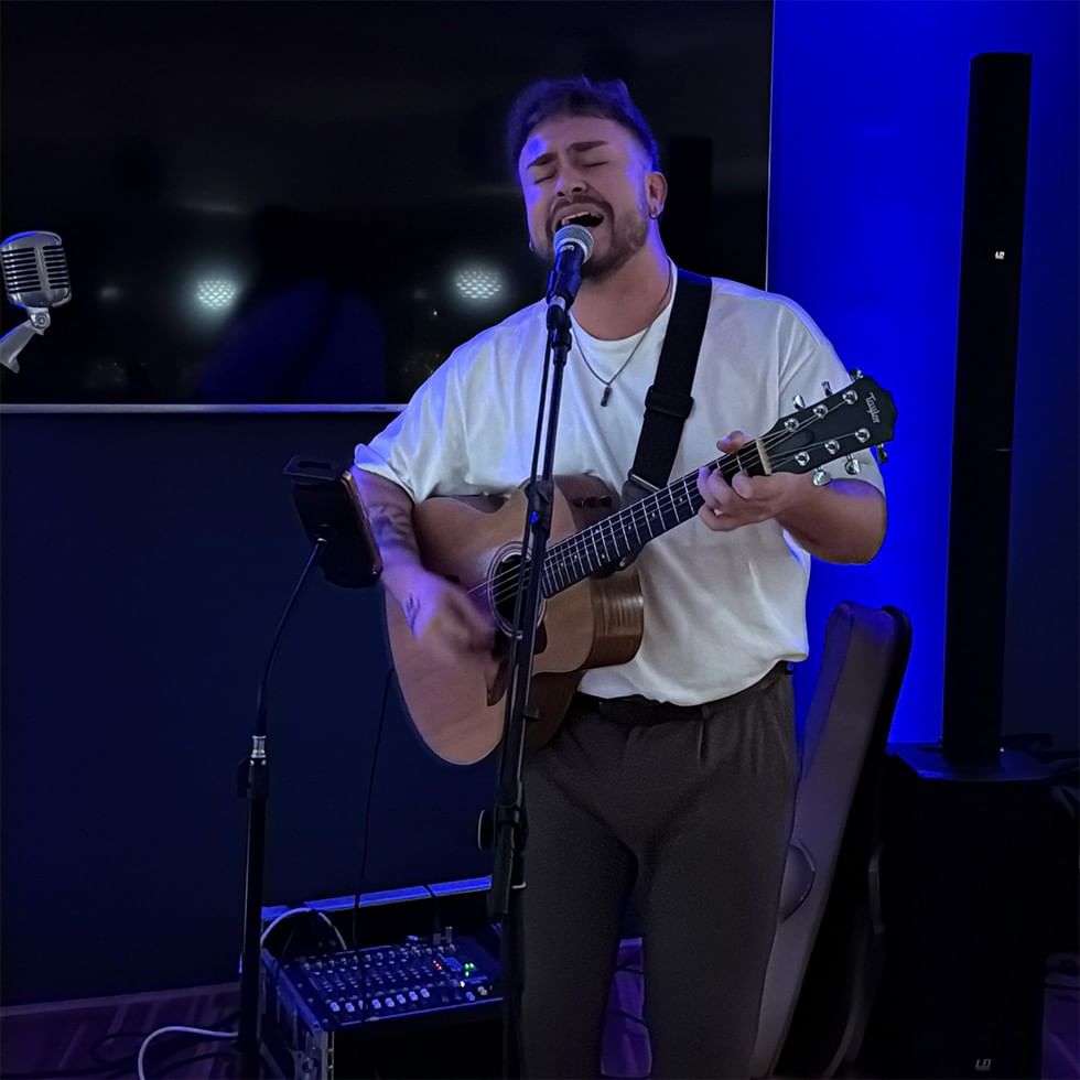 Uomo che suona chitarra e canta in un microfono a un evento.